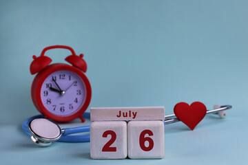 July 26. White wooden calendar blocks with date, clock and stethoscope on blue pastel background. Selective focus. health concept