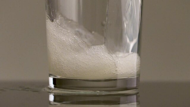Filling glass with soda water in slow motion. Stock footage. Close up of pouring soft drink with many bubbles inside the transparent glass.
