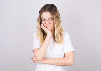pretty girl in black glasses touching her face and bending over, peeking out from under her eyes, hating talking to a boring person, standing against a gray background