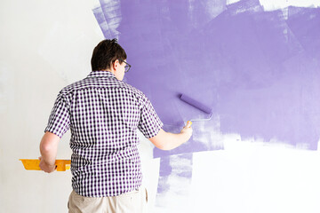 man coloring wall with roller with purple paint