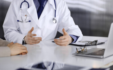 Unknown male doctor and patient woman discussing something while sitting in clinic and using clipboard. Best medical service in hospital, medicine, pandemic stop