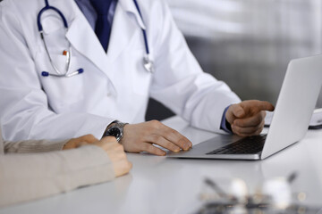 Unknown male doctor and patient woman discussing something while sitting in clinic and using laptop. Best medical service in hospital, medicine, pandemic stop