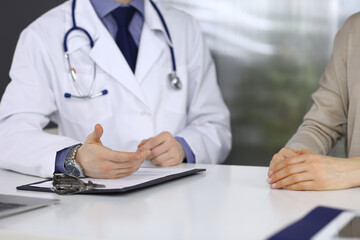 Unknown male doctor and patient woman discussing something while sitting in clinic. Best medical service in hospital, medicine, pandemic stop
