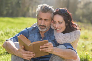 Happy couple reading a book together outdoors laying on a blanket
