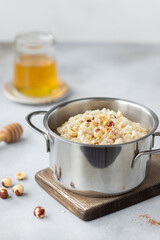 pan with delicious oatmeal porridge with hazelnuts and cinnamon. healthy breakfast. vertical image. Gray background.