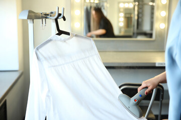 Woman holds a steam generator for steaming a white shirt in her hand