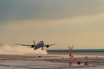 小雪舞う空港を雪煙を上げながら離陸する航空機