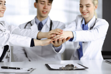 Group of doctors joining hands as a circle and ready to help patients while sitting at the desk in modern hospital office. Successful teamwork in medicine, Coronavirus countering concept