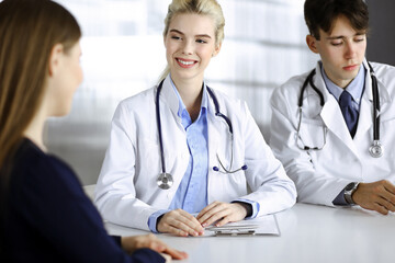 Woman-doctor with male colleague are consulting patient woman while sitting at the desk in modern clinic. Perfect medical service, medicine concept