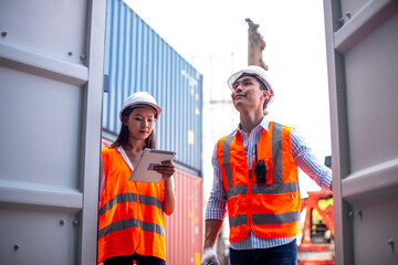 Asian dock control man and woman logistics worker wear safety helmets and protect suite open cargo container door  and working and checking product with taplets and scan code gun..