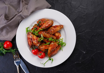barbecue chicken wings in a white plate on a dark background. Buffalo wings decorated with greens and cherry tomatoes