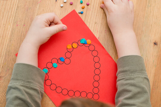making Valentines greeting card for mummy. little boy applying play dough on printed paper heart. fine motor skills, finger coordination. early education for babies