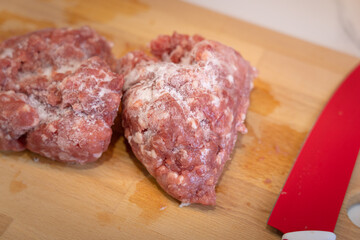 A piece of frozen chopped pork meat on the wooden cutting board, prepare for cooking in the kitchen. Food close-up and selective focus photo.