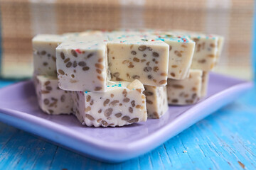 Samarkand halva cut into rhombuses with pistachios and cashews and blue and red pastry topping on a purple rectangular plate. Selective focus. Close up