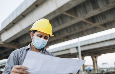 Asian construction workers wear masks and holding blueprints at construction sites.