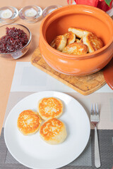 sweet cottage cheese pancakes in a plate and a clay pot, with jam on a server table Delicious cottage cheese dessert