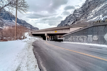 Highway road passing under a bridge against rocky mountain and cloudy sky views