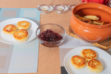 sweet cottage cheese pancakes in a plate and a clay pot, with jam on a server table Delicious cottage cheese dessert