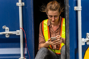 Fototapeta na wymiar Caucasian worker sitting in container box and using smart phone when her break