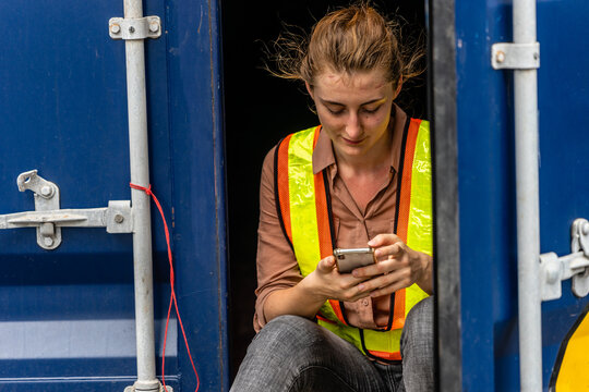 Caucasian worker sitting in container box and using smart phone when her break - Powered by Adobe
