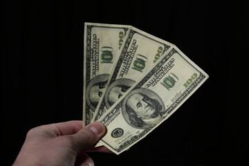 Hand holds one hundred dollar bills on black background