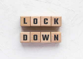 Text LOCK DOWN made of wood cubes on white textured putty background. Travel restrictions related to the COVID-19 pandemic. Stay home. Social interaction. Coronavirus concept.