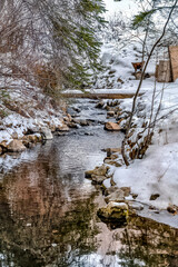 Snowy hill landscape in winter with narrow rocky stream amid thriving trees
