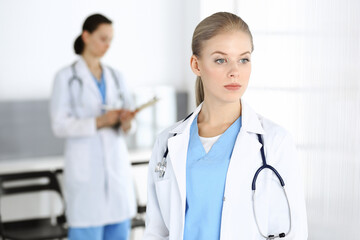 Woman - doctor standing in clinic with colleague at the background. Physician at work. Medicine and health care concept