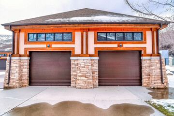 Hip roof garage exterior with two brown doors and wet snowy driveway in winter. © Jason