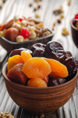 Dried dates and apricots in clay bowl on wooden kitchen table closeup