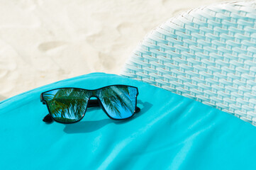Blue sunglasses on turquoise fabric on the beach. Reflection of the palm trees