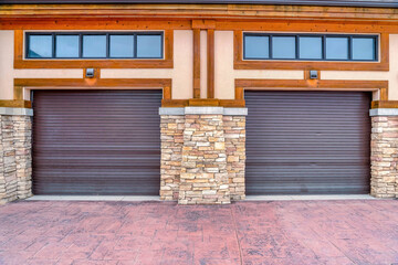 Two car garage with glass windows above brown doors between stone pillars