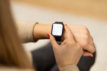 Smartwatch on girls hand with blank screen mock-up for your design at home office sitting on the couch near green plant with blurry background with free space for custom text