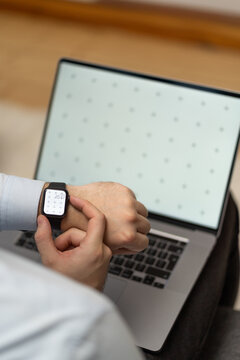 Businessman with smartwatch on hand with blank screen mock-up for your design at home office sitting on the couch with blurry background with free space for custom text