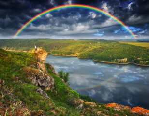 rainbow over the river. woman on a cliff above the canyon
