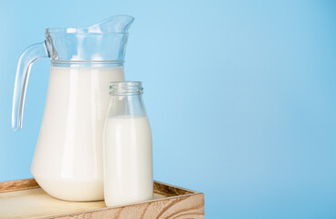 jug and bottle of fresh milk glass on wooden crate box on a blue background. Raw milk is high in calcium and protein to drink for all ages. Milk consumption nutritious and healthy dairy products.