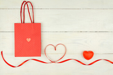 Creative Valentine Day romantic composition with red hearts, satin ribbon and paper bag on wooden background. Mockup with copy space for blogs and social media.