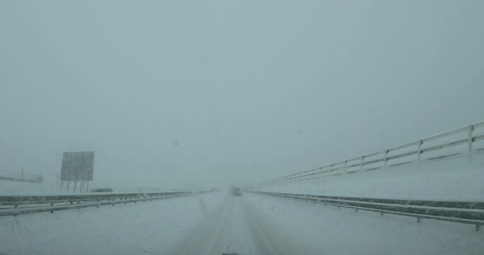 Dashcam dash camera POV slow driving on snowy highway road in Slovenia. Snowstorm in winter season. Snow covering motorway in blizzard. Forward dolly moving, wide angle, real time