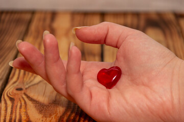 A female hand on a wooden background holds a heart...