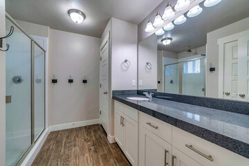 Shower stall with sliding glass door in front of sink mirror and wall lamps
