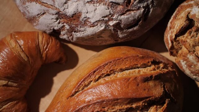 Different kinds of organic bread and a croissant on a rotating wood background. Baked whole-wheat bread in a traditional German bakery. Tasty and healthy food. Top-down view, macro, 4K. 