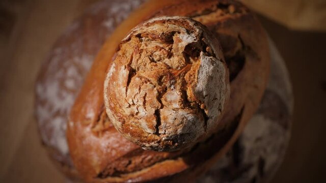 Rotating close up of organic whole wheat bread on a wood background. Different kinds of delicious fresh homemade bread loaves and a bun on top of each other. 4K.
