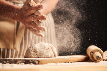 Mains de boulanger femelle faisant de la pâte à pain avec un tablier. Rouleau et planche à découper visibles en arrière-plan. Ingrédients naturels faits maison. Fond sombre, étalonnage des couleurs marron.