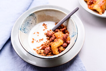 Healthy breakfast yogurt bowl with granola and caramelized bananas and nuts on grey concrete background. Selective focus
