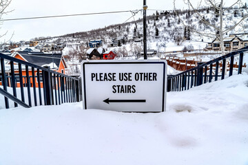 Please Use Other Stairs sign on an impassable stairway in the snowy neighborhood