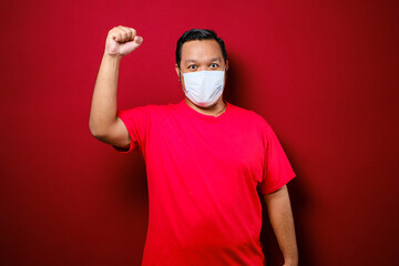 Young asian man wearing a medical face mask while raise his hand up to encourage and protects against the spread of corona virus disease
