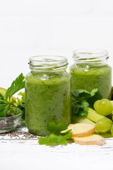 green fruit and vegetable smoothies in jars on white table, vertical