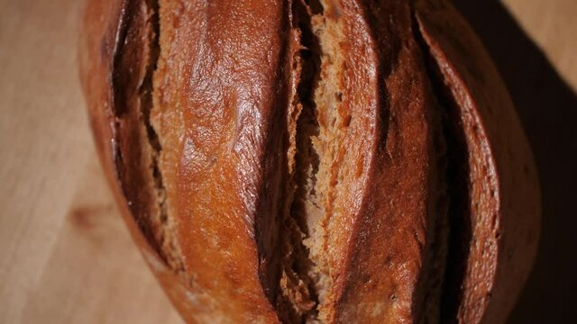 Close-up of a fresh, homemade and organic bread loaf with textured rustic crust. Baked whole-wheat bread in a traditional German bakery. Tasty and healthy food. Rotating top-down view, macro, 4K.