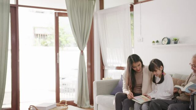 Wide Shot : Multi Generational Asian Family Sitting On Sofa At Livingroom. Father And Mother Teaching And Reading Book For Daughter Activity In Holiday Time. Big Family Spending Time In Living Room