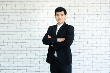 portrait of  young asian businessman in suit arm crossed standing and smile with white brick background.